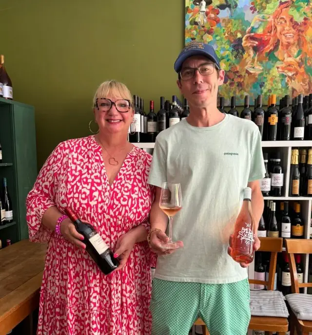Christina und Christian, die Gastgeber des Weingold, mit Weinflasche und Glas im Laden