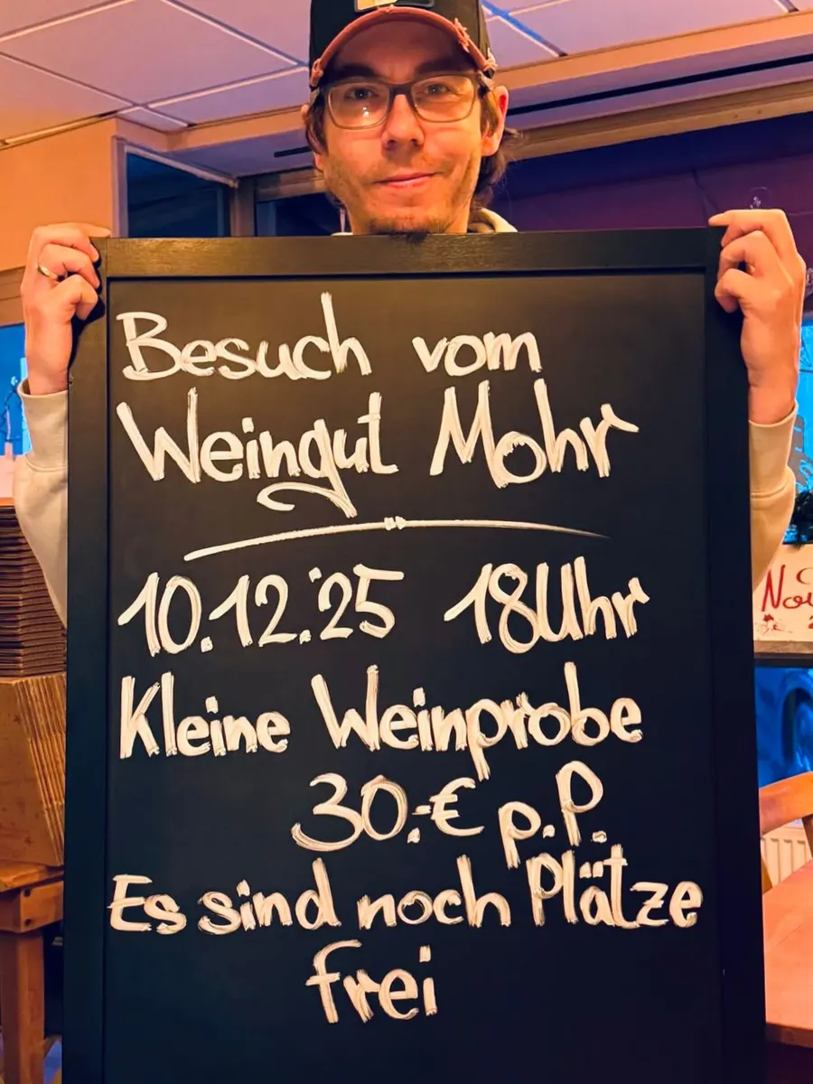 Christian hält eine Kreidetafel hoch, die eine kleine Weinprobe mit dem Weingut Mohr ankündigt