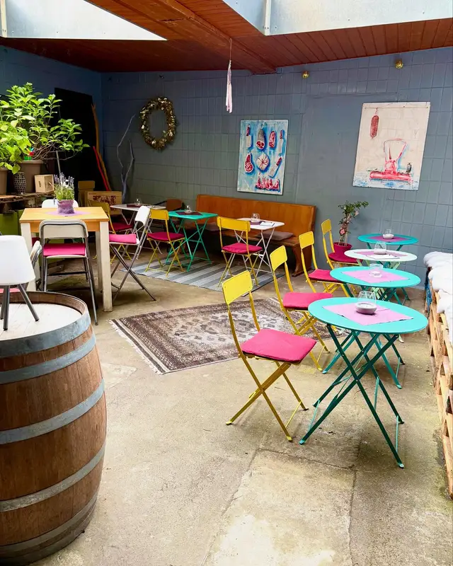 Der bunte Weinhof des Weingold: türkise Bistrotische, pinke und gelbe Klappstühle, Teppiche und ein Weinfass